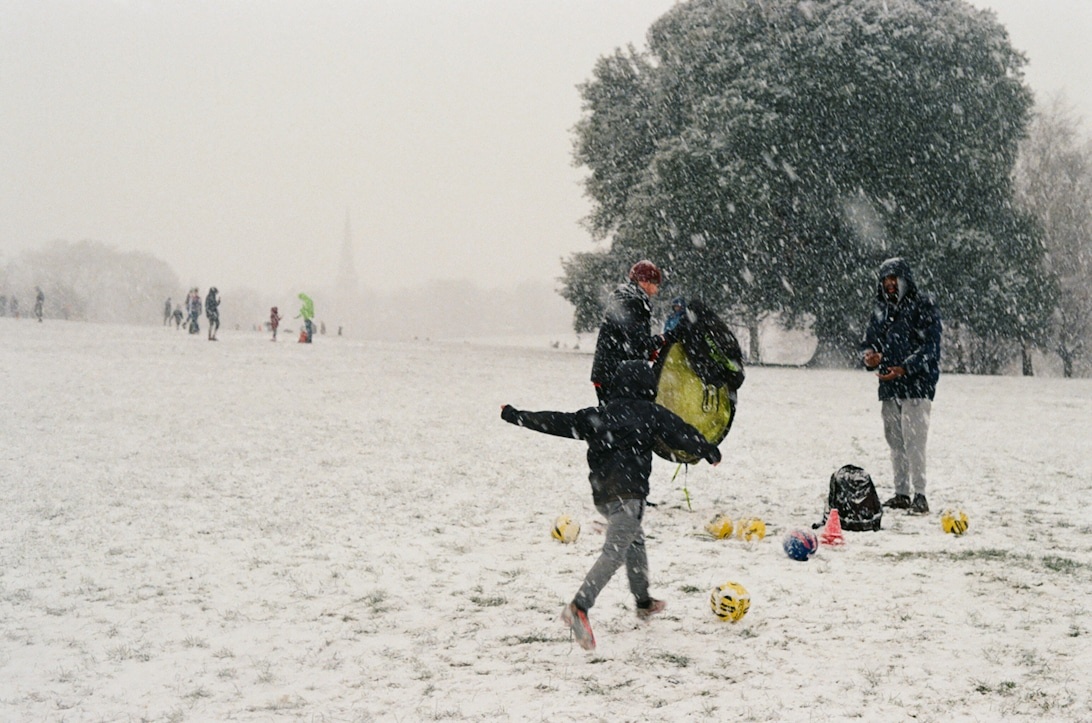 Fotbollsspelare som tränar i kraftigt snöfall på en plan med gula markörer.